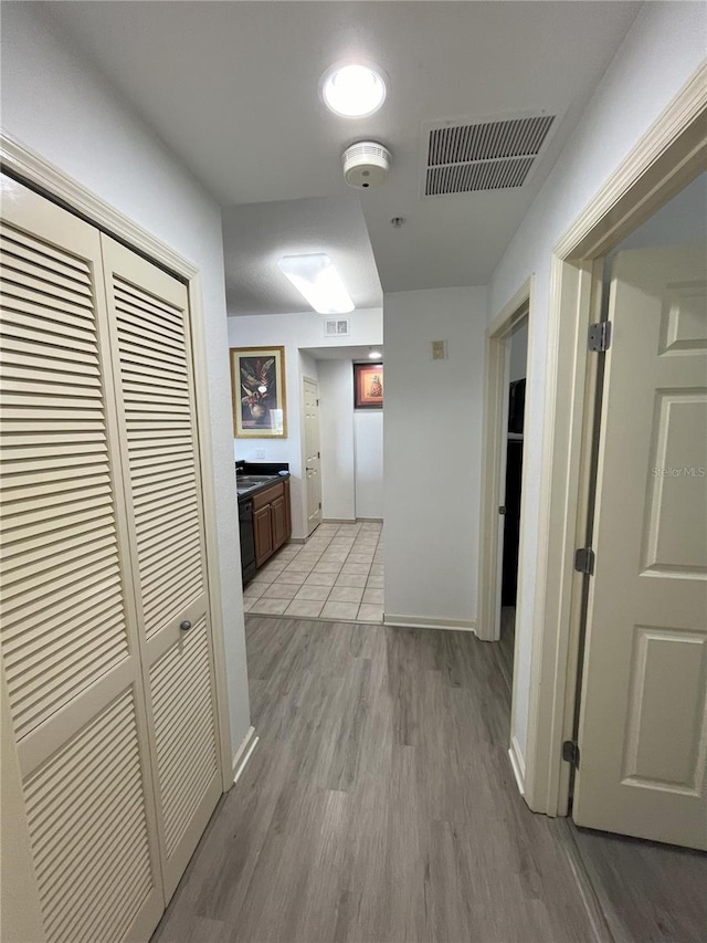 corridor with light wood-type flooring, visible vents, and baseboards