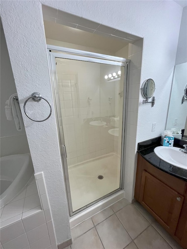 full bathroom featuring a textured wall, tiled bath, tile patterned flooring, vanity, and a stall shower