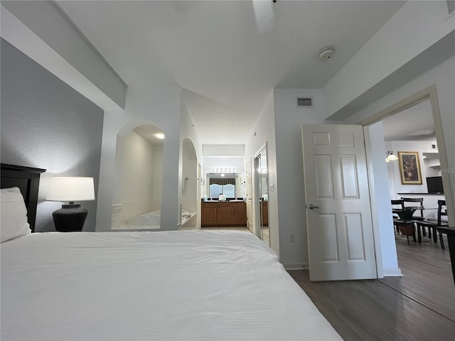 bedroom with connected bathroom, arched walkways, visible vents, and dark wood finished floors