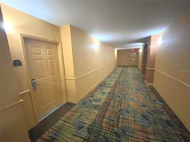 corridor featuring baseboards and dark colored carpet