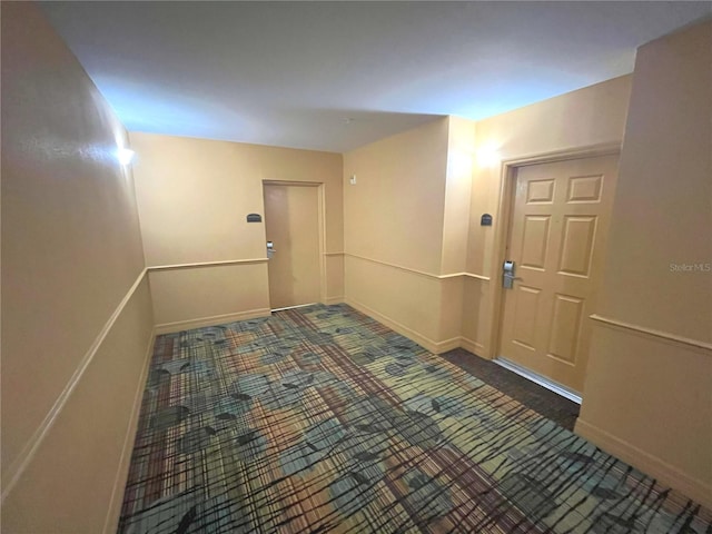 hall with dark colored carpet and baseboards