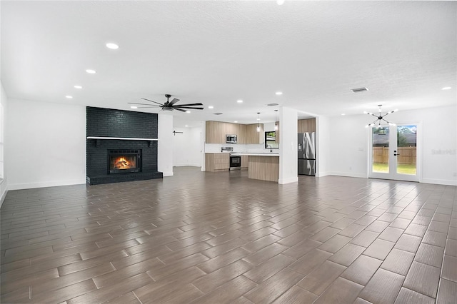 unfurnished living room featuring ceiling fan, french doors, a fireplace, and brick wall