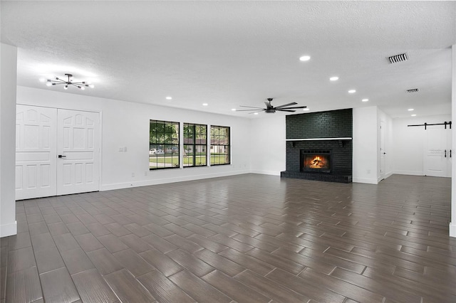 unfurnished living room featuring a textured ceiling, ceiling fan, a barn door, a brick fireplace, and brick wall