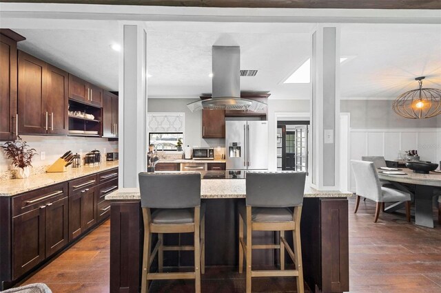 kitchen with appliances with stainless steel finishes, hanging light fixtures, island range hood, dark wood-type flooring, and a kitchen island