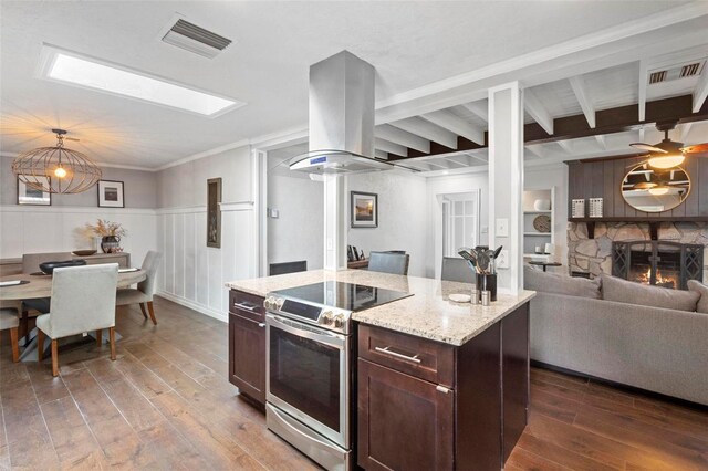 kitchen with light wood-type flooring, a fireplace, island exhaust hood, beam ceiling, and stainless steel range with electric cooktop