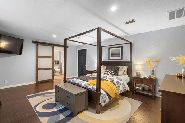 bedroom featuring a barn door, dark hardwood / wood-style floors, and ensuite bathroom