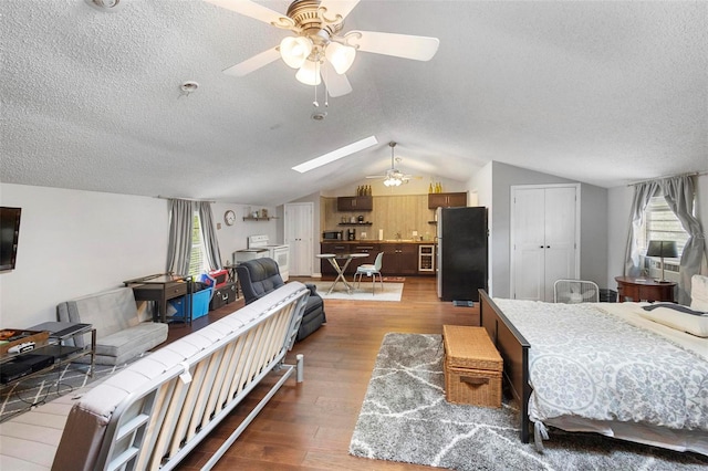 bedroom featuring vaulted ceiling with skylight, wood-type flooring, black fridge, and ceiling fan