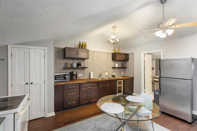 kitchen featuring ceiling fan with notable chandelier, a textured ceiling, appliances with stainless steel finishes, vaulted ceiling, and dark hardwood / wood-style flooring