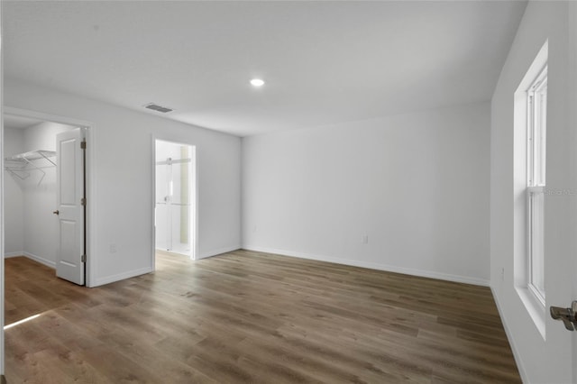 unfurnished bedroom with a walk in closet, a closet, and dark wood-type flooring