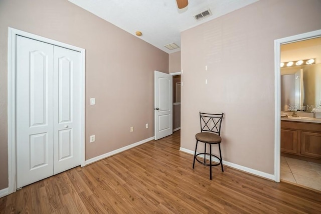 bedroom with ensuite bath, a closet, light wood-type flooring, and ceiling fan