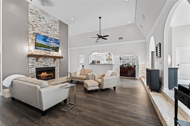 living room featuring a stone fireplace, crown molding, high vaulted ceiling, dark hardwood / wood-style flooring, and ceiling fan