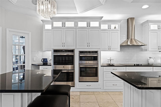 kitchen featuring wall chimney exhaust hood, white cabinetry, a center island, double oven, and decorative backsplash