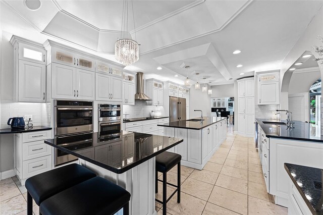 kitchen featuring white cabinets, a raised ceiling, wall chimney exhaust hood, and a kitchen island