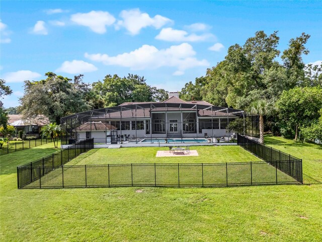 back of property with a patio, a fenced in pool, glass enclosure, and a lawn