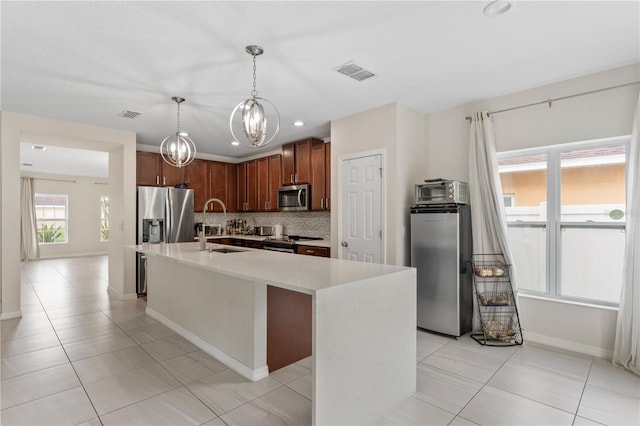 kitchen with light tile patterned floors, appliances with stainless steel finishes, tasteful backsplash, and a center island with sink