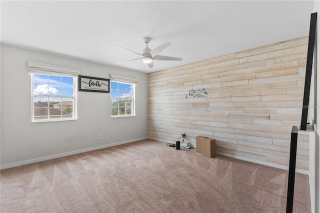 carpeted spare room with wood walls and ceiling fan