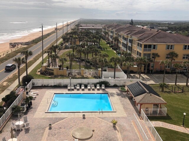 view of pool featuring a patio, a water view, a beach view, and a lawn