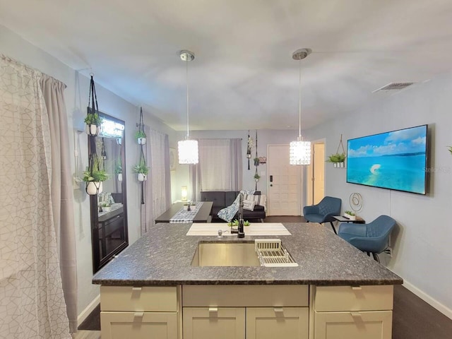 kitchen with a center island with sink, cream cabinets, and dark stone countertops