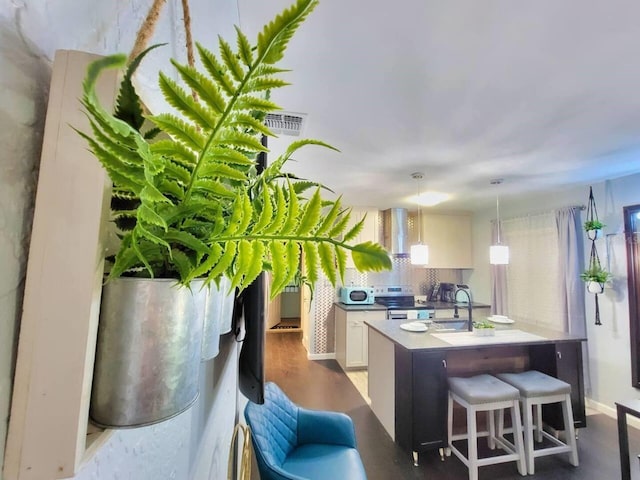 kitchen featuring sink, a center island with sink, pendant lighting, stainless steel electric stove, and white cabinets