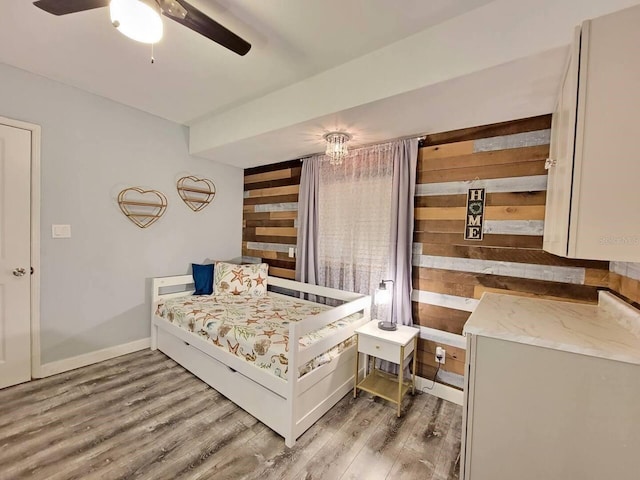 bedroom featuring hardwood / wood-style flooring, ceiling fan, and wooden walls