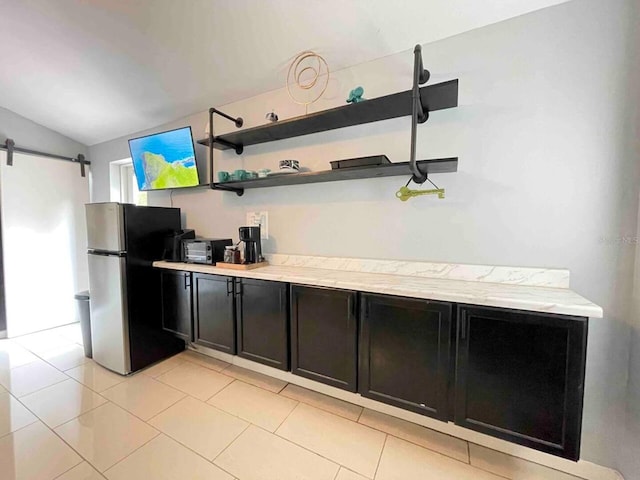 kitchen featuring vaulted ceiling, a barn door, light tile patterned floors, and stainless steel refrigerator