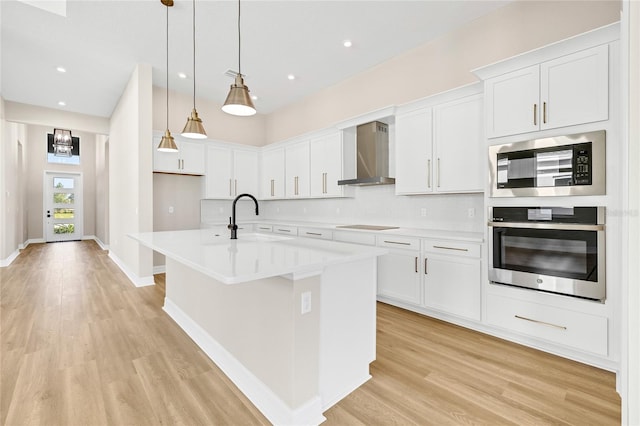 kitchen with sink, stainless steel appliances, wall chimney exhaust hood, white cabinets, and a center island with sink