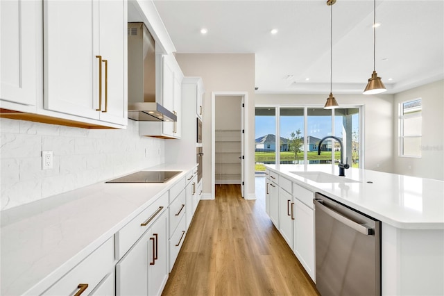 kitchen with black electric stovetop, wall chimney range hood, sink, dishwasher, and hanging light fixtures