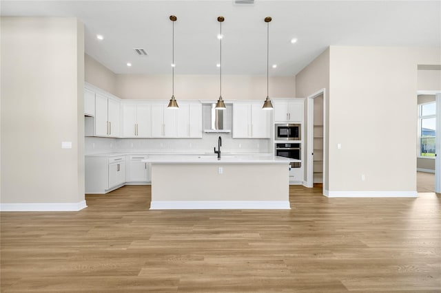 kitchen with light wood-type flooring, an island with sink, and white cabinets