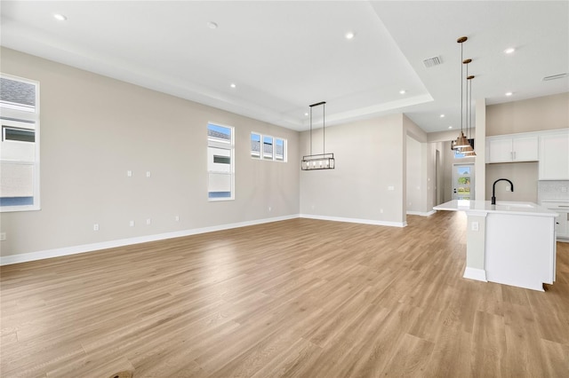 unfurnished living room featuring an inviting chandelier, sink, light wood-type flooring, and a raised ceiling