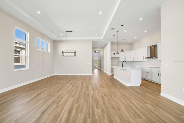 unfurnished living room featuring light hardwood / wood-style floors, a raised ceiling, sink, and a chandelier