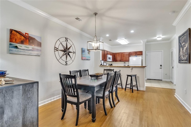 dining room with crown molding, light wood-type flooring, and an inviting chandelier