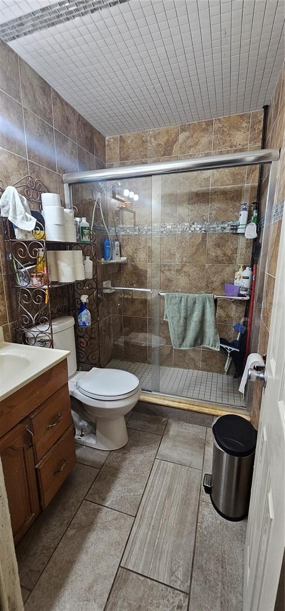 bathroom featuring toilet, tile patterned flooring, tile walls, an enclosed shower, and vanity