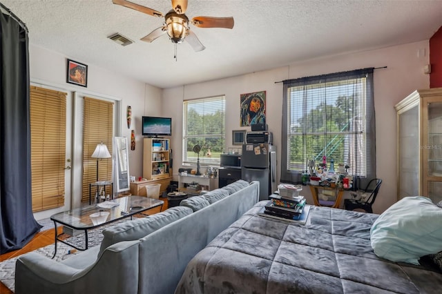 bedroom with ceiling fan, a textured ceiling, stainless steel fridge, and hardwood / wood-style floors