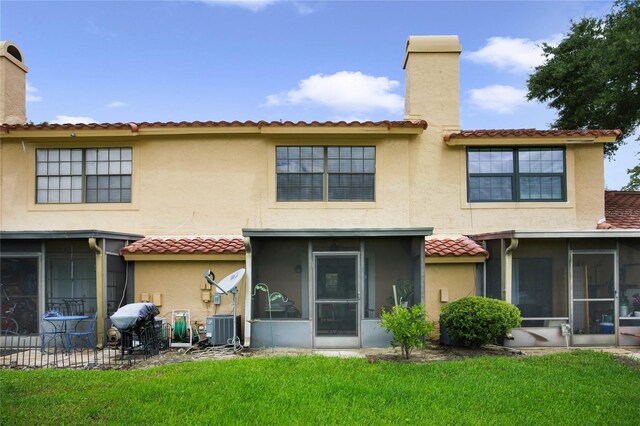 rear view of property with central air condition unit, stucco siding, a yard, a sunroom, and a chimney