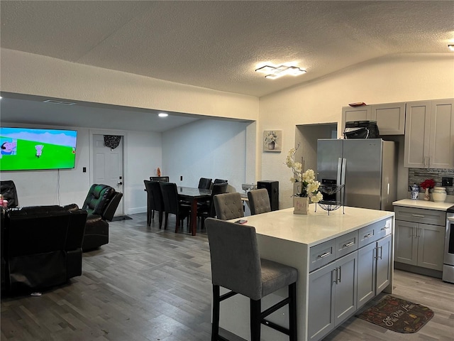 kitchen featuring stainless steel appliances, wood finished floors, a kitchen breakfast bar, light countertops, and gray cabinets