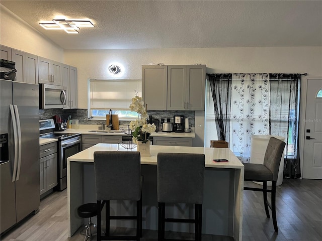 kitchen with appliances with stainless steel finishes, a center island, gray cabinets, light countertops, and a sink