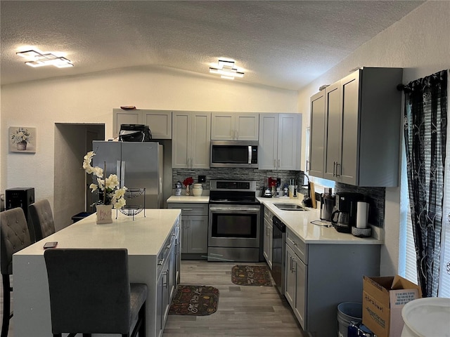 kitchen with light countertops, appliances with stainless steel finishes, a sink, and gray cabinetry