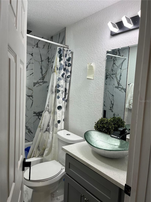 full bathroom featuring toilet, vanity, a textured ceiling, and a textured wall