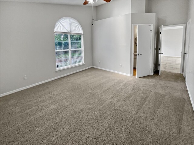 unfurnished bedroom with light carpet, ensuite bath, ceiling fan, and a towering ceiling