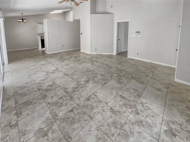 tiled empty room featuring ceiling fan with notable chandelier and a towering ceiling