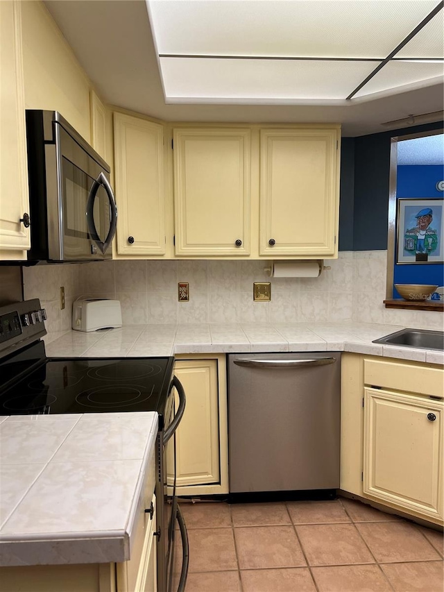 kitchen featuring light tile patterned flooring, backsplash, appliances with stainless steel finishes, and cream cabinets