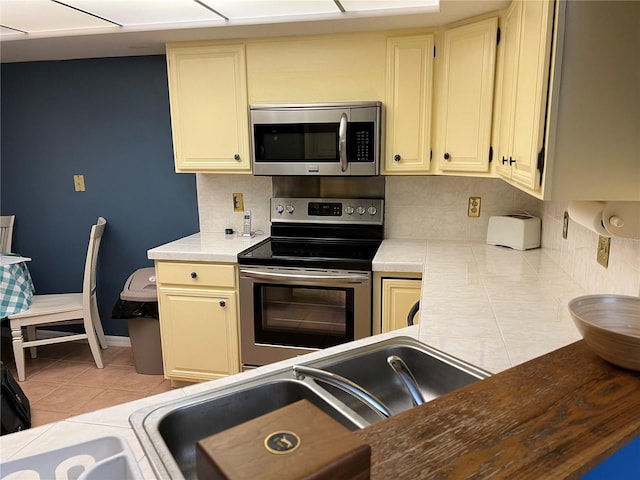 kitchen with tasteful backsplash, light tile patterned flooring, cream cabinetry, and stainless steel appliances