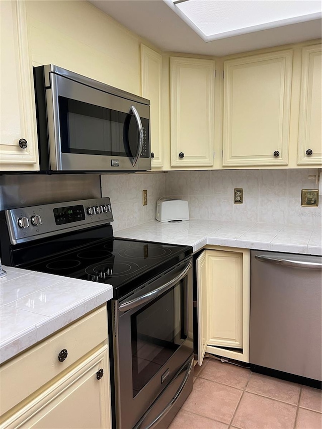 kitchen featuring appliances with stainless steel finishes, cream cabinetry, light tile patterned floors, and tasteful backsplash