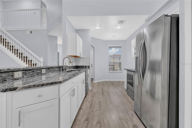 kitchen featuring appliances with stainless steel finishes, white cabinets, dark stone countertops, light wood-type flooring, and sink