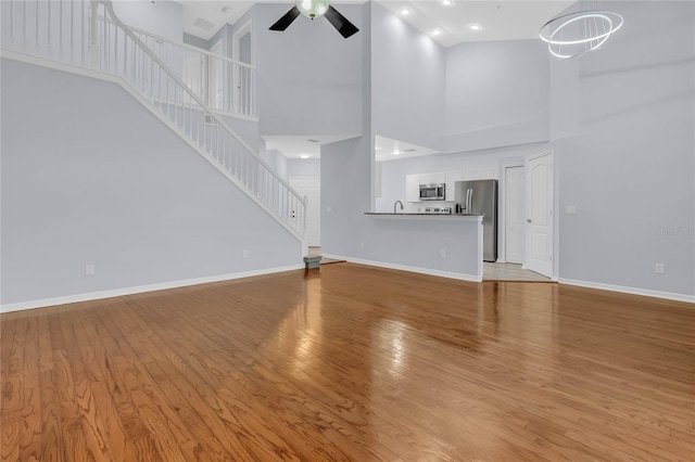 unfurnished living room featuring high vaulted ceiling, ceiling fan, and light hardwood / wood-style floors