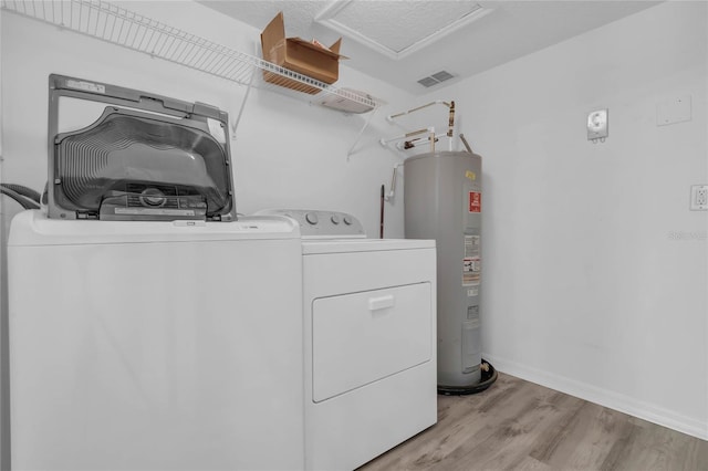 washroom featuring washing machine and clothes dryer, light hardwood / wood-style flooring, and electric water heater