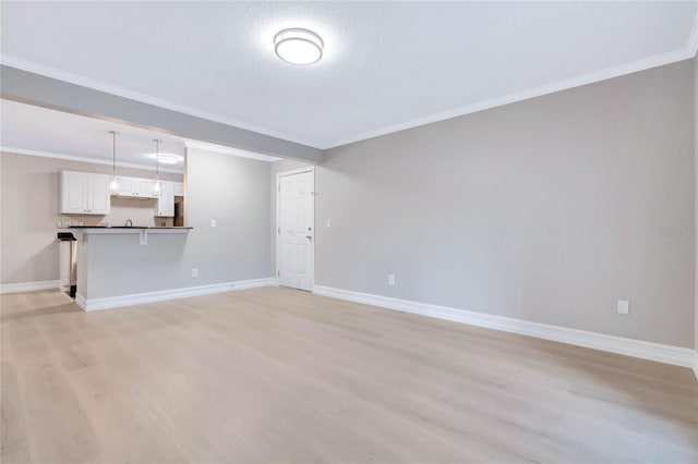 unfurnished living room with ornamental molding, light wood-type flooring, and baseboards