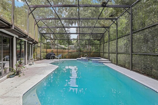 view of swimming pool with glass enclosure, an in ground hot tub, and a patio area