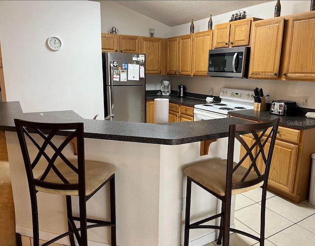 kitchen with light tile patterned flooring, stainless steel appliances, a kitchen breakfast bar, and lofted ceiling