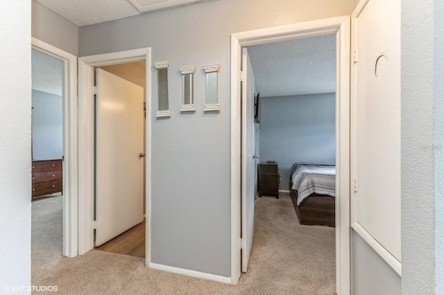 hall with baseboards, a textured ceiling, and light colored carpet